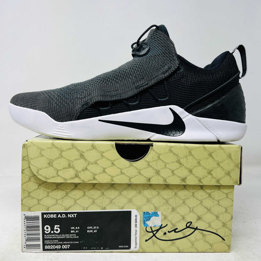 A pair of Nike Kobe A.D. NXT Black White sneakers rests on a box. These shoes boast clean black uppers, contrasting white soles, and the iconic Nike swoosh. The box, labeled with size 9.5, features a signature on the front.