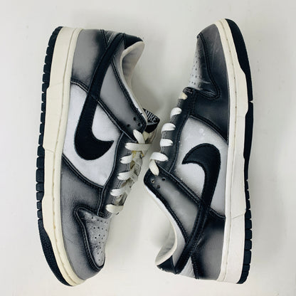 The Nike Dunk Low Haze 2003 features black and white sneakers with bold black swoosh logos, complemented by black laces, white midsoles, and black outsoles, showcased side by side on a plain white backdrop.