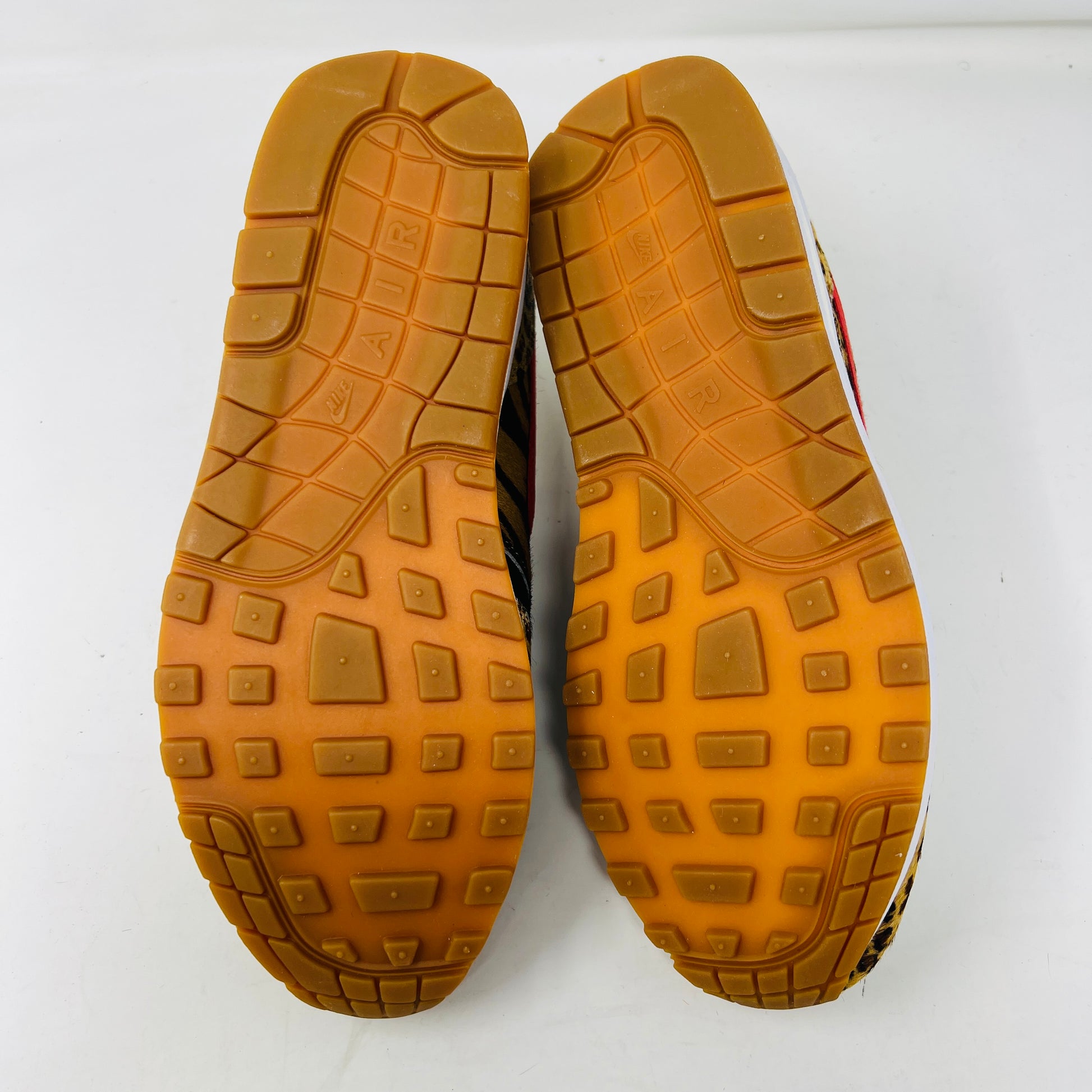 The image displays the waffle tread soles of Nike Air Max 1 Atmos Animal Pack 2.0 shoes, colored in brownish-orange with AIR visible on each sole, positioned side by side on a white surface.