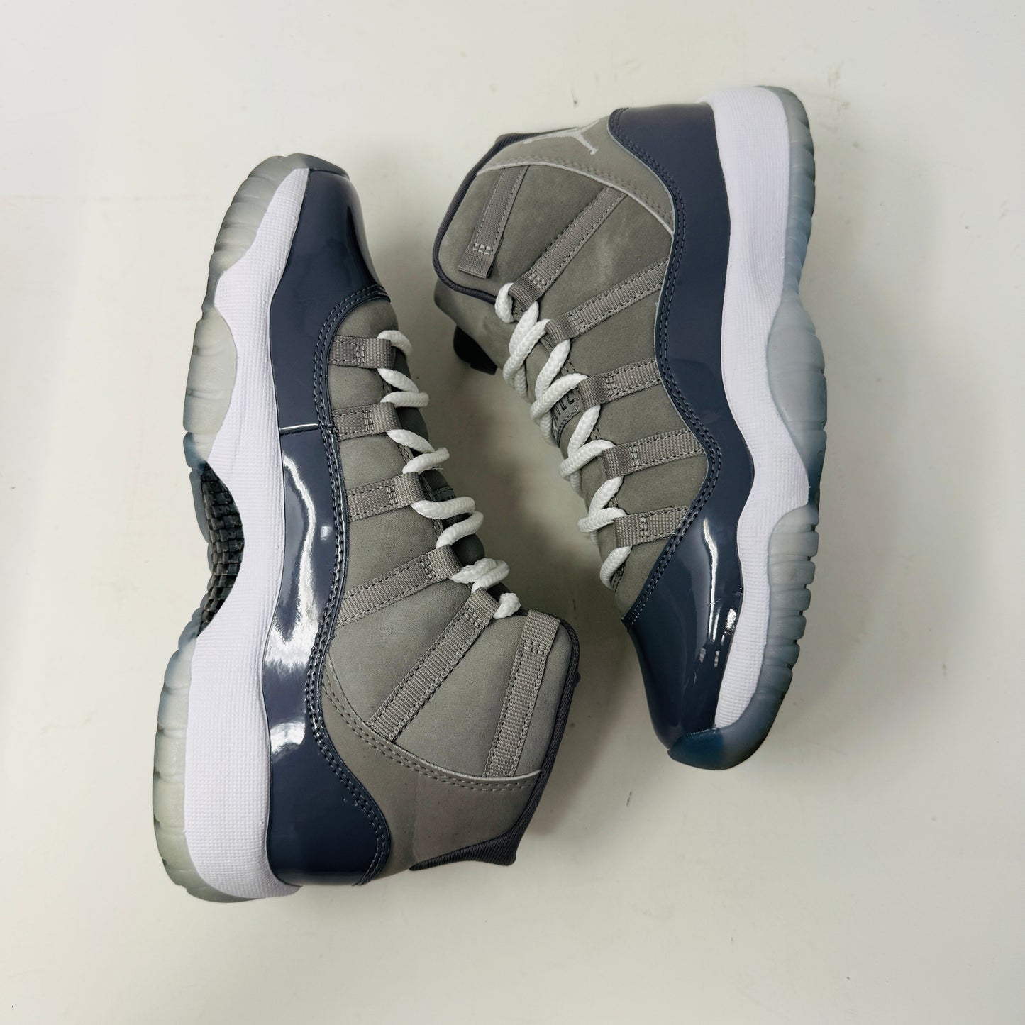 The Jordan 11 Retro Cool Grey (2021) (GS) sneakers by Jordan feature glossy patent leather overlays, a Jumpman logo on the heel, clean white uppers, and laces. They are displayed on a pristine Nike shoebox with size and model details labeled.