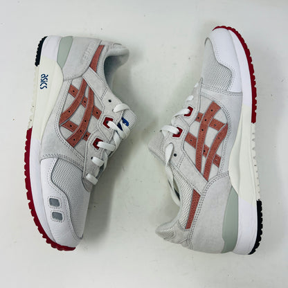 The ASICS Gel-Lyte III Ronnie Fieg Tokyo Trio Yoshino Rose sneaker, featuring clean white and beige uppers with red accents and pink iconic stripes, sits on its box. It includes navy, pink, and beige extra laces, with the authentic size clearly displayed on the box.