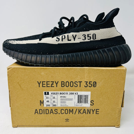 Brand new adidas Yeezy Boost 350 V2 Core Black White sneakers with SPLY-350 text rest on a pristine Yeezy box. The mint condition box displays sizing info and branding details.