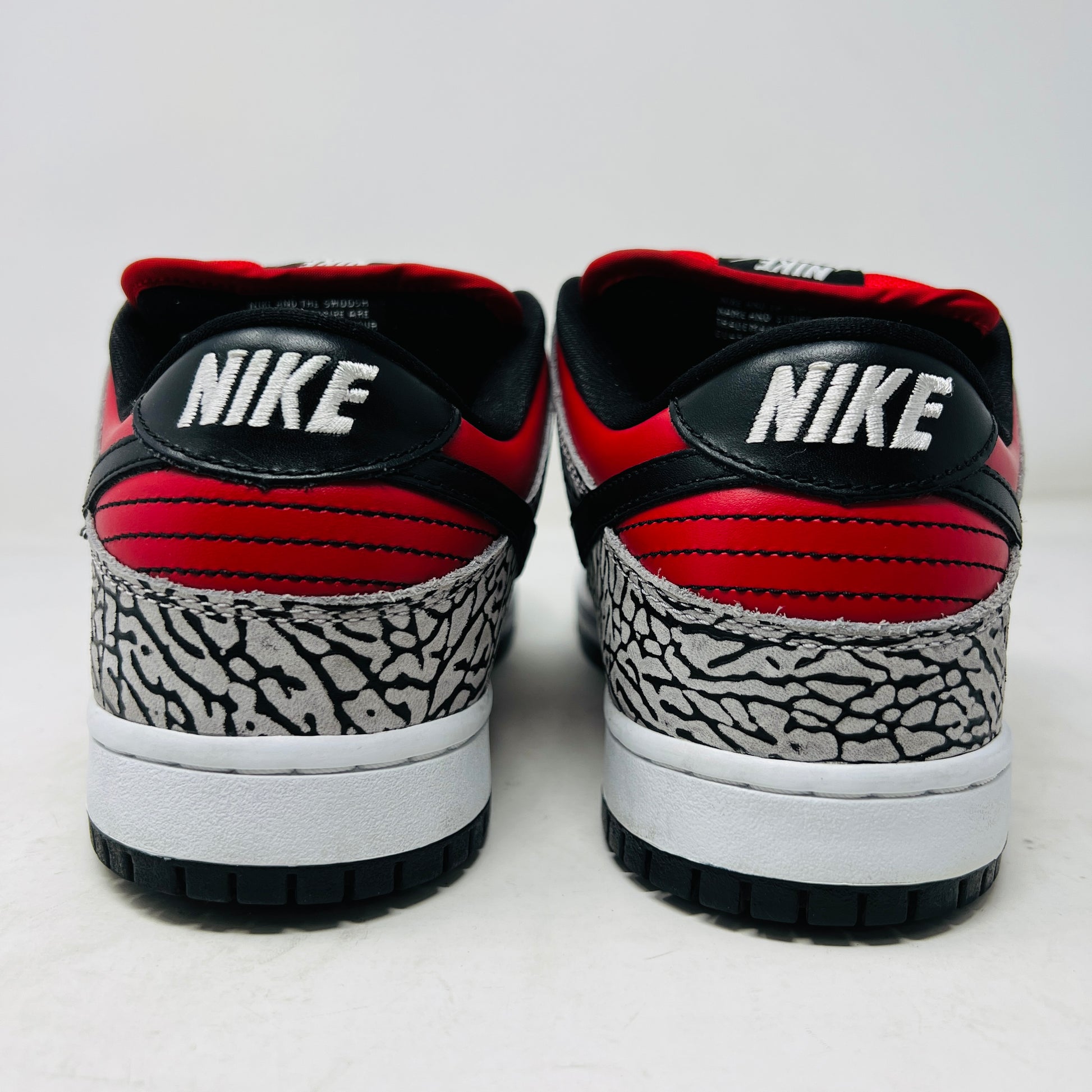 A genuine Nike SB Dunk Low Supreme Red Cement (2012) sneaker, featuring red and black elephant print details, rests on a cardboard box and comes with extra white laces for added style versatility.