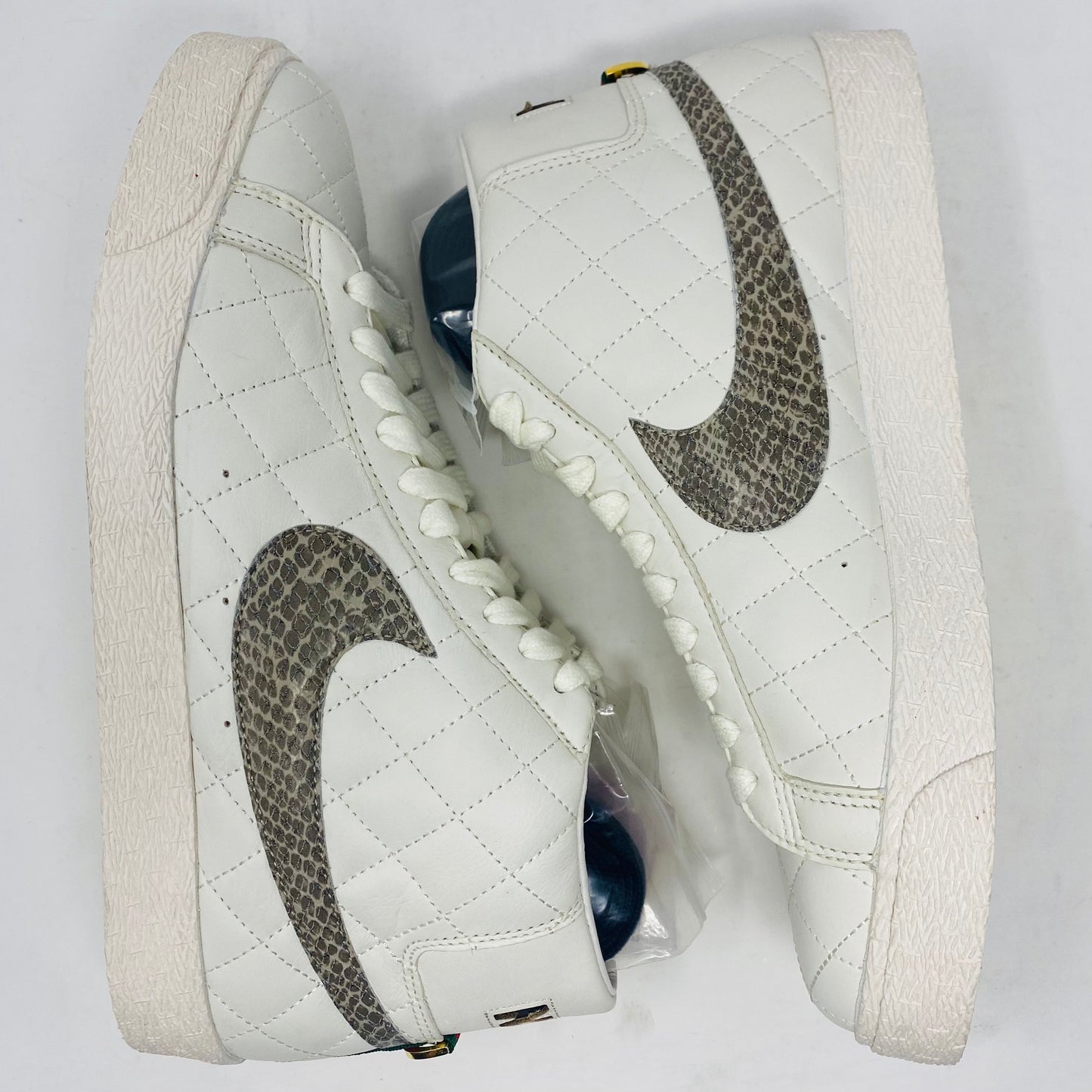 Nike SB Supreme Blazer White 2006 features a quilted high-top design with snakeskin-patterned swooshes, white laces, and a textured rubber sole. These sneakers are displayed on a white background.