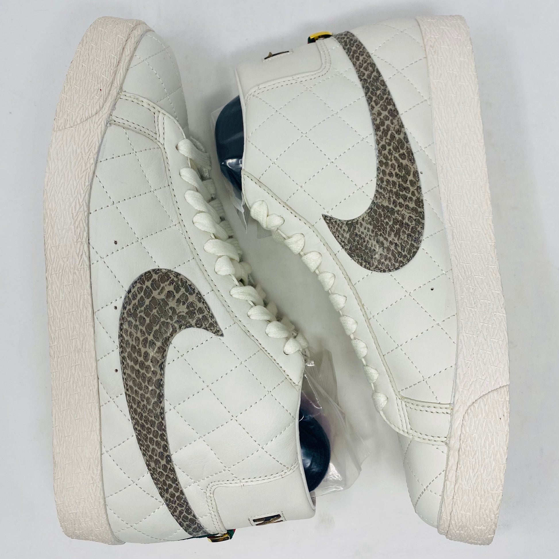 Nike SB Supreme Blazer White 2006 features a quilted high-top design with snakeskin-patterned swooshes, white laces, and a textured rubber sole. These sneakers are displayed on a white background.