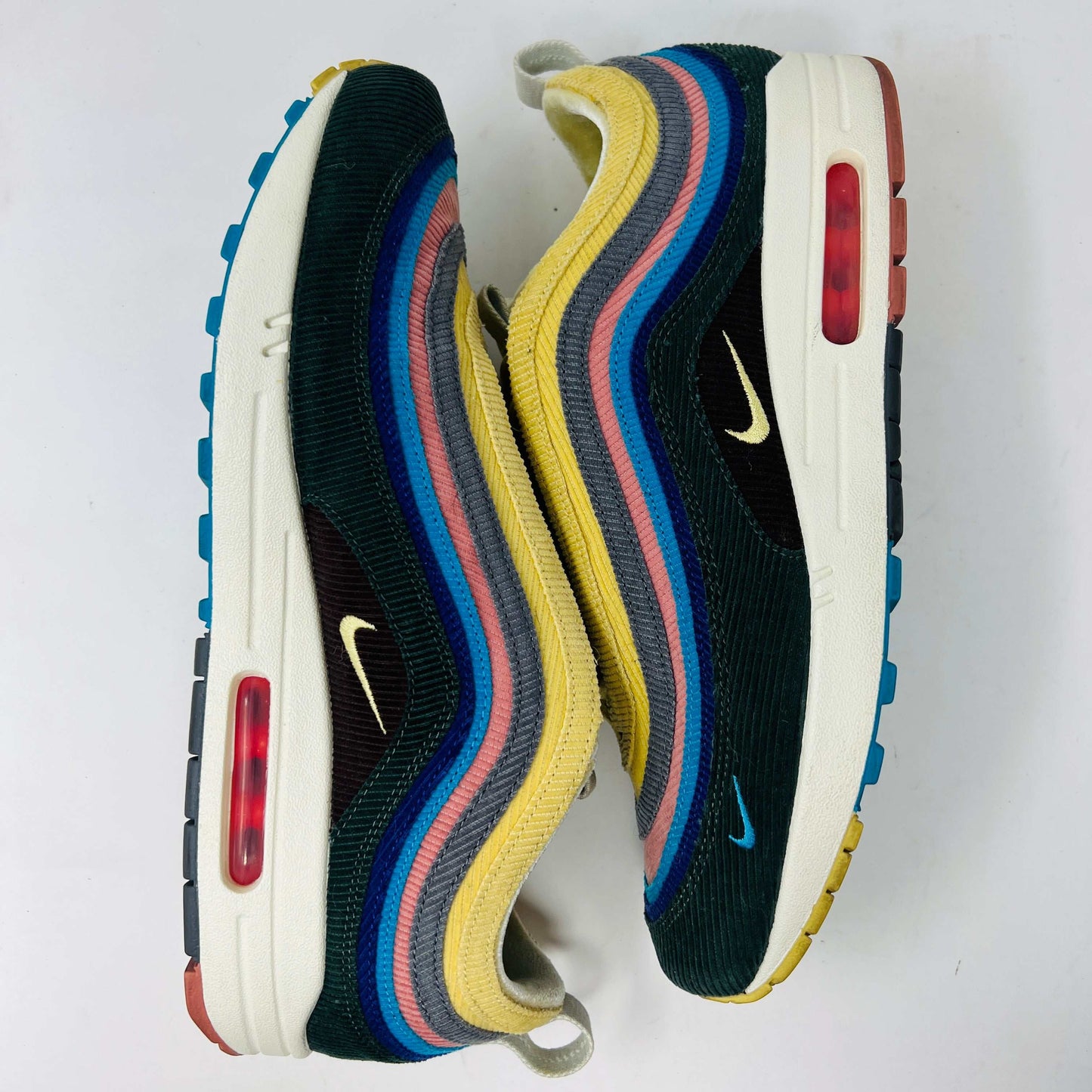 The Nike Air Max 1/97 Sean Wotherspoon sneakers, from Nike, feature a blend of blue, pink, yellow, and black patterns with a textured design. They include a visible air unit in the midsole, a prominent swoosh logo on the side, extra laces, and blue-detailed soles.