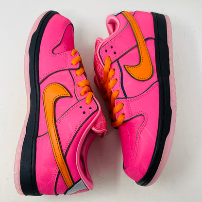 Nike SB Dunk Low The Powerpuff Girls Blossom sneakers feature vibrant pink with orange swoosh logos and laces, black soles, and embody Blossoms playful charm, all against a white backdrop.