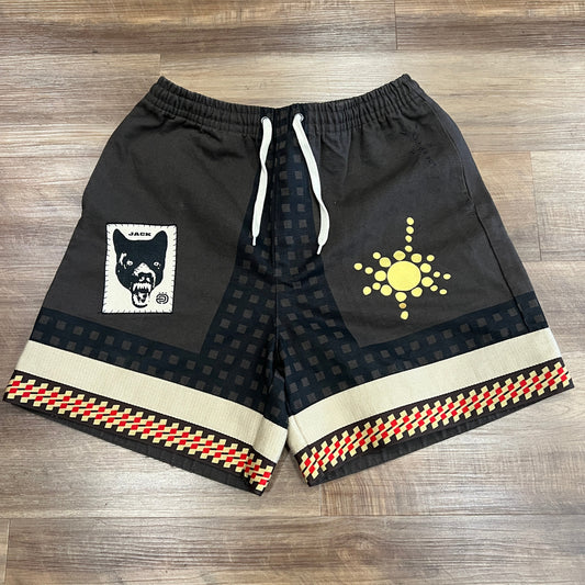 These brand new Travis Scott Cactus Jack Wolf Short Multi in medium feature a dogs face graphic on the left leg and a yellow sun-like emblem on the right. The hem has a red, yellow, and white checkered pattern, perfectly contrasted against a wooden floor backdrop.