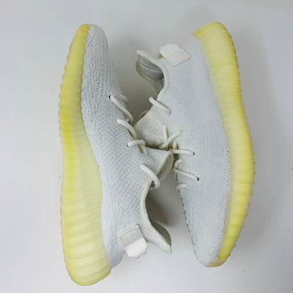 A pair of Yeezy Boost 350 V2 Cream sneakers, featuring textured fabric and light yellow translucent soles, are set against a plain white background to display top and side views.