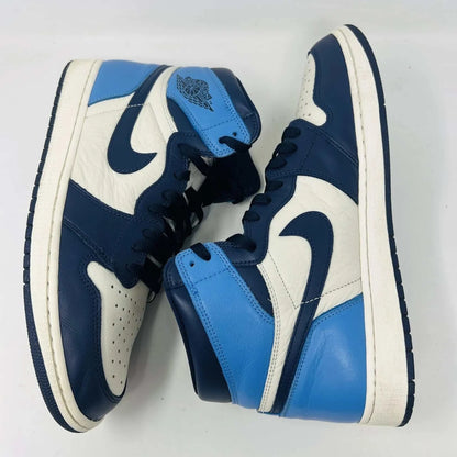 The Jordan 1 Retro High Obsidian sneakers, featuring a blue, white, and black design with signature swoosh and Air Jordan branding on the ankle, are gracefully displayed on a black Nike box with a red logo. A bag of blue shoelaces accompanies the 2019 release from Jordan.