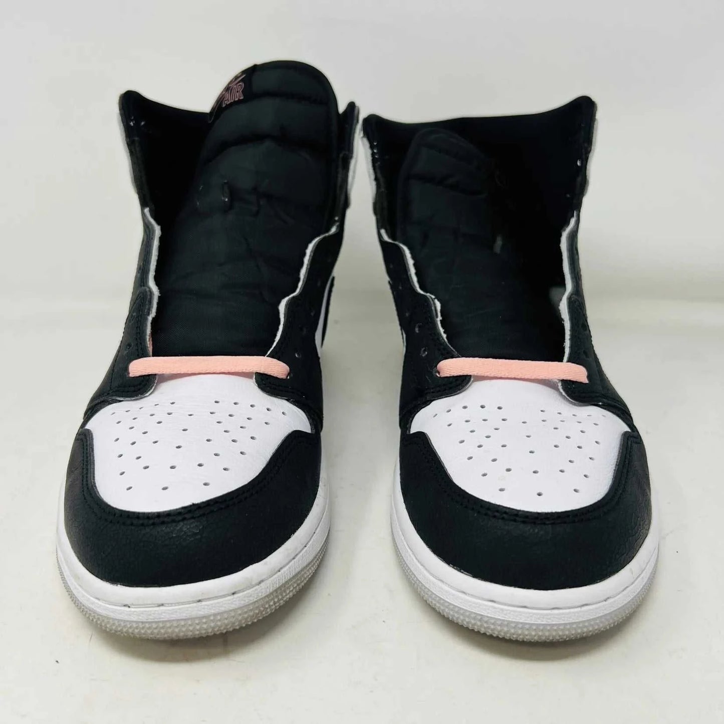 The Jordan 1 Retro High OG Bleached Coral sneaker by Jordan features a high-top design with a clean white base, prominent black Nike swoosh, gray detailing on the heel, and the iconic Jordan wings logo near the ankle. Its set against a plain background.