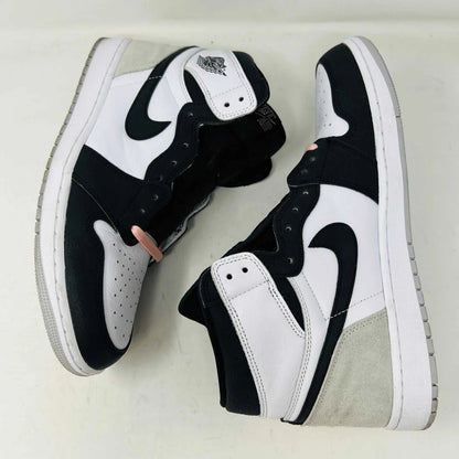 The Jordan 1 Retro High OG Bleached Coral sneaker by Jordan features a high-top design with a clean white base, prominent black Nike swoosh, gray detailing on the heel, and the iconic Jordan wings logo near the ankle. Its set against a plain background.