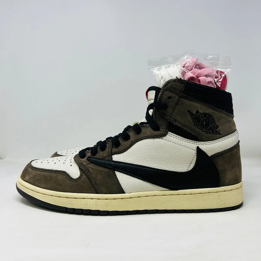 The Jordan 1 Retro High OG SP Travis Scott Mocha, by Jordan, is a high-top sneaker featuring 100% authentic white and brown suede panels with a black reverse swoosh. Its set against a plain white background and includes extra pink and cream laces in clear plastic on top.