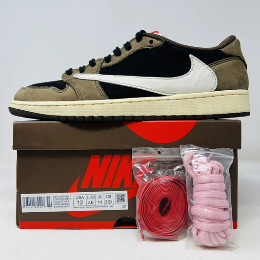 The Jordan 1 Retro Low OG SP Travis Scott Mocha sneakers, released in 2019 and featuring brown, black, and white tones, are displayed on a Nike box. Two extra lace sets, one red and one pink, are included in plastic bags beside the box.