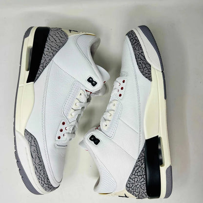 An authentic Jordan 3 Retro White Cement Reimagined sneaker with gray elephant print accents sits on its black Nike Air shoebox. It has red details and black branding, with the Nike Air logo on the heel and tongue. Released in 2023, box shows size 13.