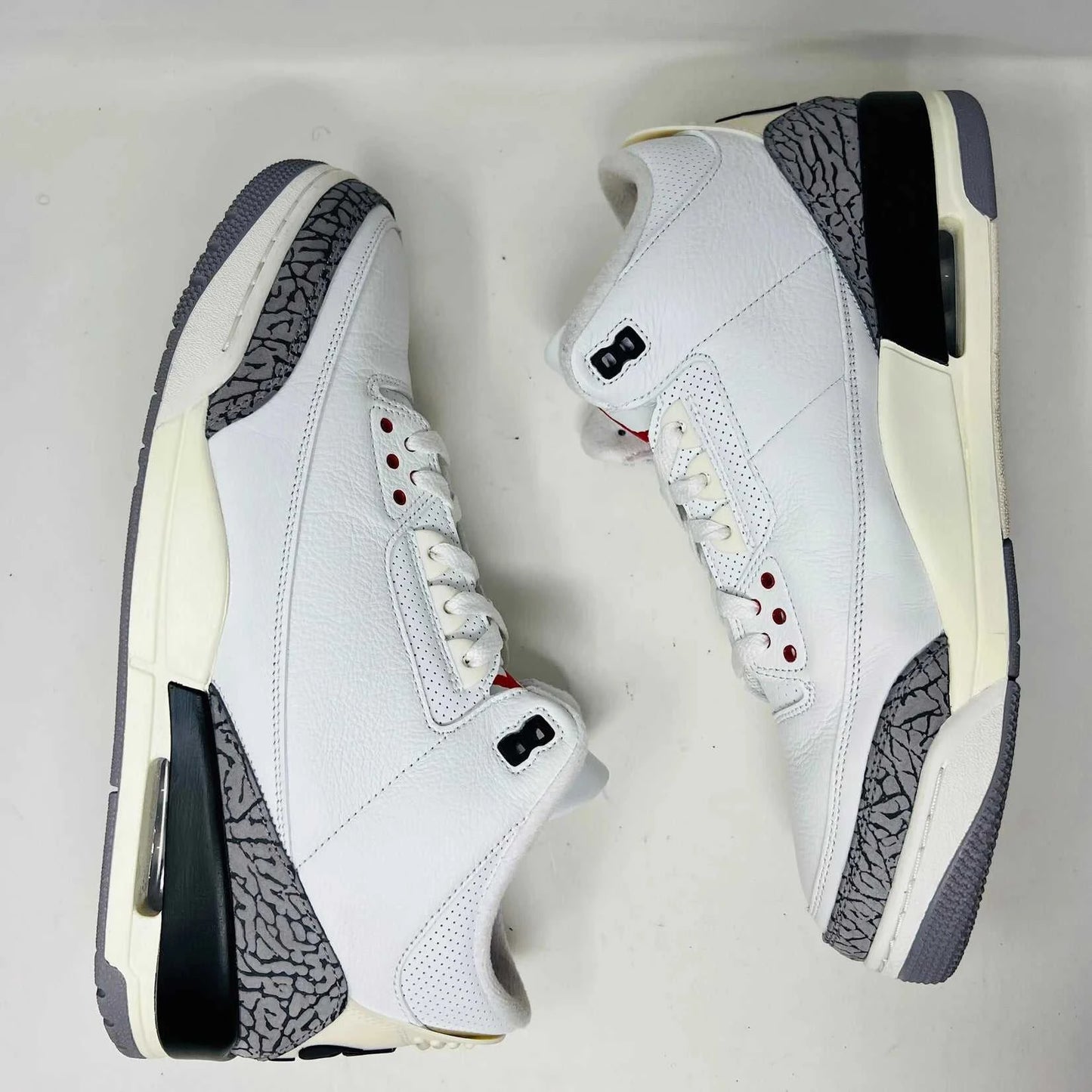 An authentic Jordan 3 Retro White Cement Reimagined sneaker with gray elephant print accents sits on its black Nike Air shoebox. It has red details and black branding, with the Nike Air logo on the heel and tongue. Released in 2023, box shows size 13.