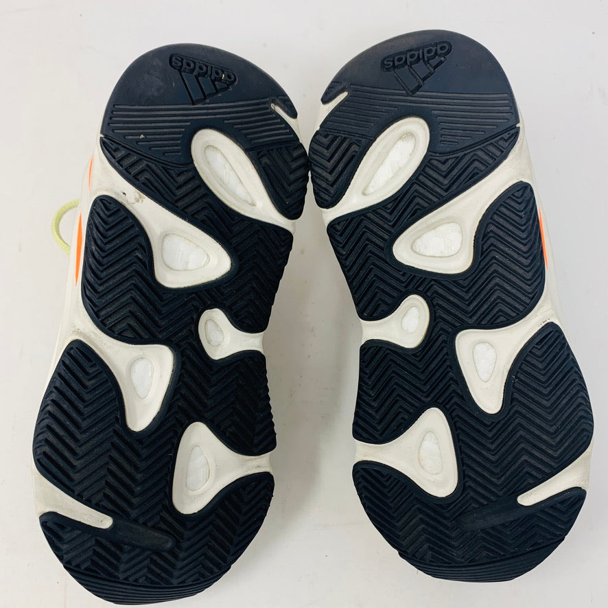 The image features the soles of a pair of Yeezy sneakers, with black, textured rubber grips and an abstract pattern. The outsoles have white and orange accents, and the Adidas logo is displayed on both heels. This model appears to be the adidas Yeezy Boost 700 Wave Runner.