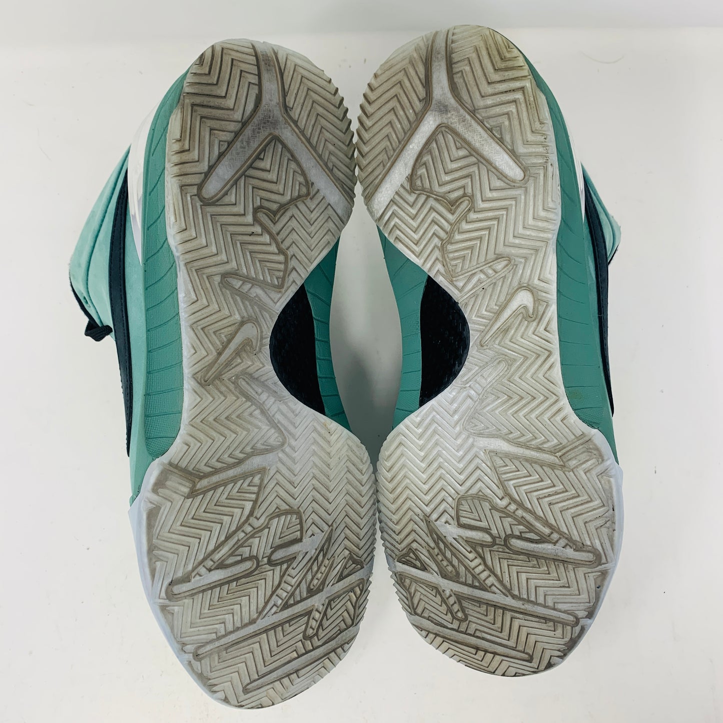 The image displays the soles of Nike Kobe 4 Protro Girl Dad athletic shoes. Featuring a herringbone tread pattern, these teal and black shoes show wear with some dirt on the soles.