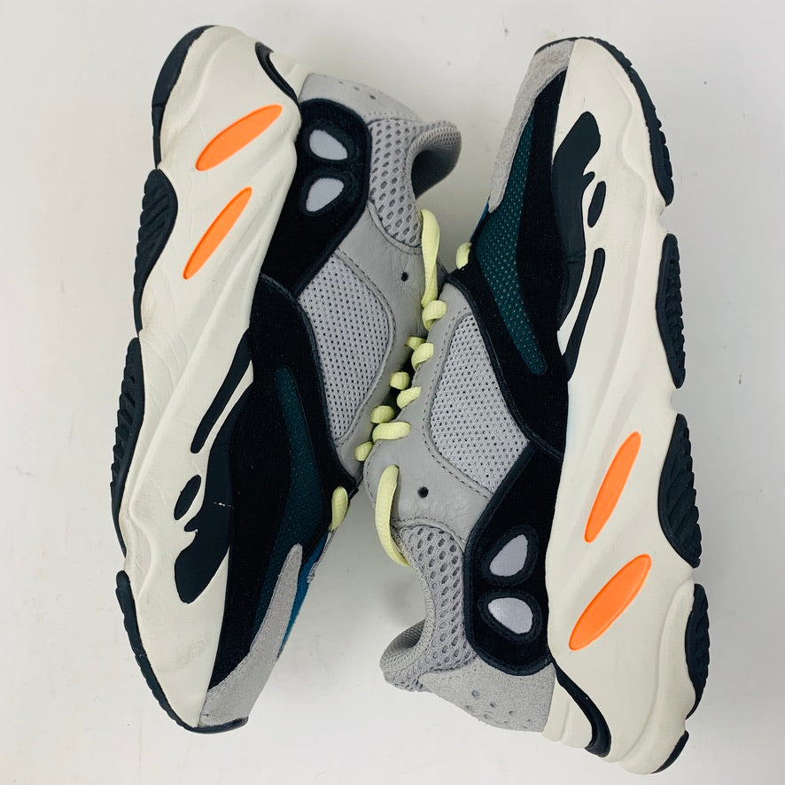 A pair of adidas Yeezy Boost 700 Wave Runner sneakers in gray and black, with white soles and orange accents, are displayed side by side on a white surface, highlighting their unique design and prominent midsoles.