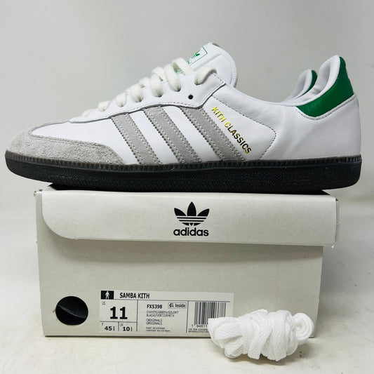 Showcased on a box are authentic adidas Samba OG Kith Classics White Green sneakers, with white uppers, gray suede accents, green detailing, and Kith Classics text. Nearby size info and crisp white laces complete the scene.