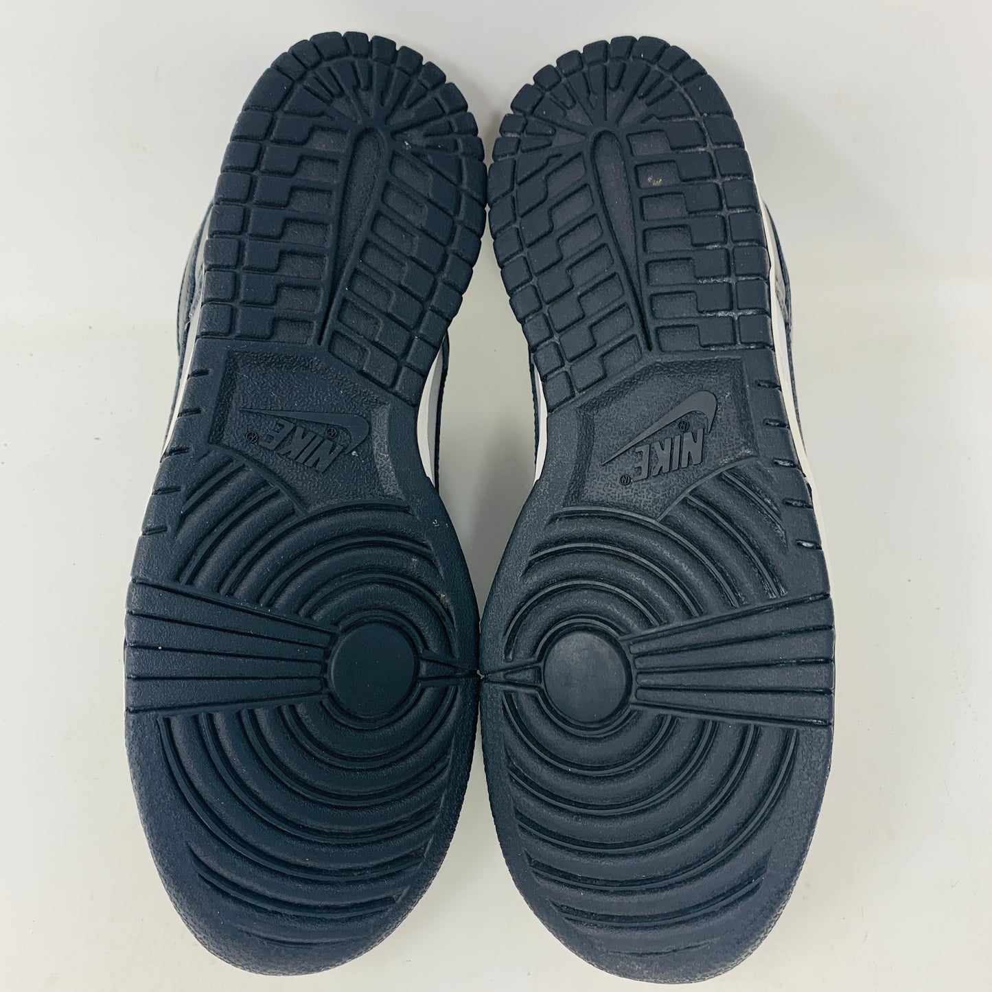 The image displays the black, circular-patterned soles of Nike Dunk Low Haze 2003 sneakers with the Nike logo visible in the tread. The shoes are positioned side by side on a white surface.