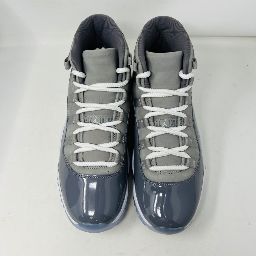 A pair of Jordan 11 Retro Cool Grey (2021) sneakers with white laces and translucent soles rest on a gray Nike Air box, showcasing the shiny patent leather and Jumpman logo. Size 9.5 appears on the label.