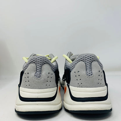 The image showcases the back view of adidas Yeezy Boost 700 Wave Runner sneakers, featuring a gray mesh upper with suede accents, black detailing, orange highlights, and a white sole against a plain white background.