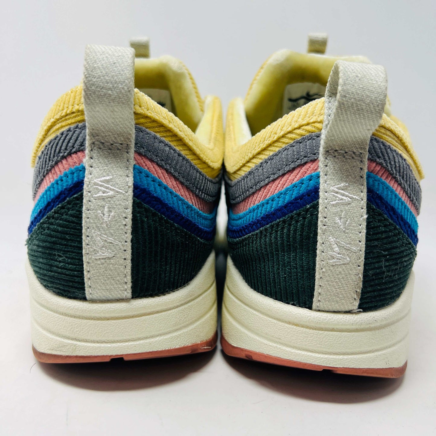 The Nike Air Max 1/97 Sean Wotherspoon sneakers, from Nike, feature a blend of blue, pink, yellow, and black patterns with a textured design. They include a visible air unit in the midsole, a prominent swoosh logo on the side, extra laces, and blue-detailed soles.