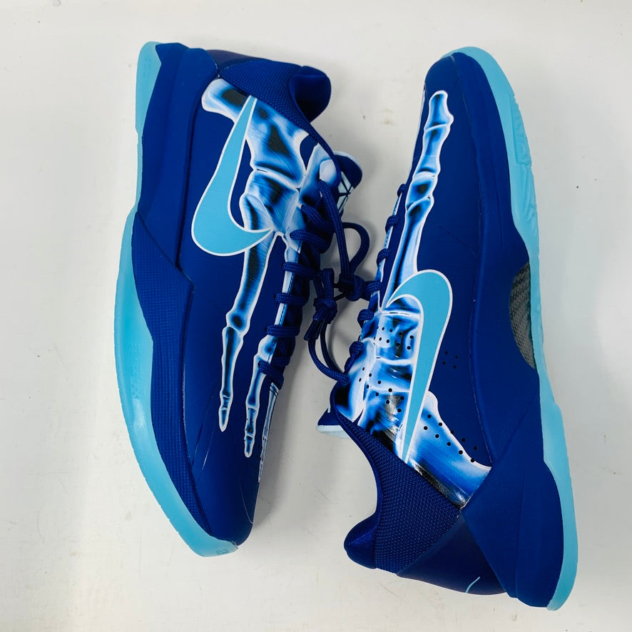 The Nike Kobe 5 Protro X-Ray athletic shoes feature bright blue soles, a white skeletal design on the sides, and a large white swoosh logo. They are showcased on a white surface.