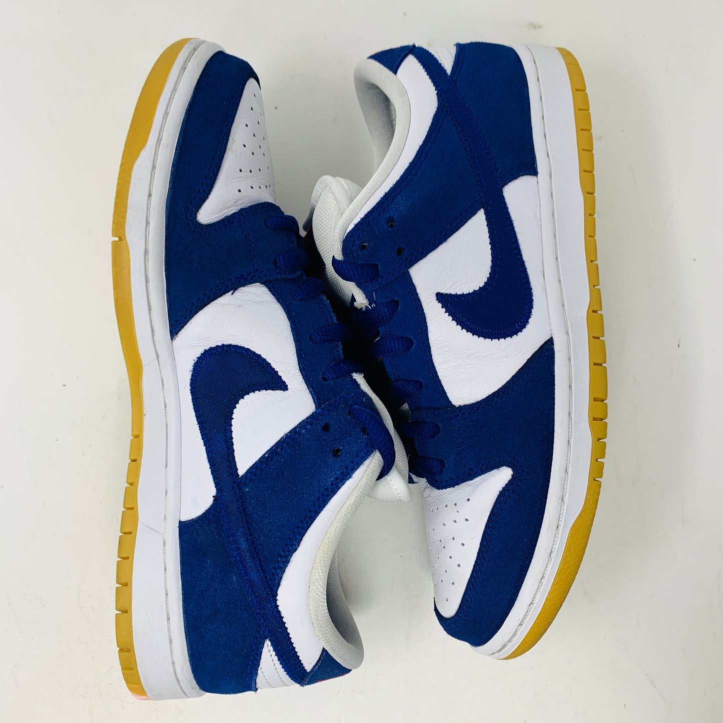 The Nike SB Dunk Low Los Angeles Dodgers showcases a 2022 design with a white and blue color scheme, featuring the iconic swoosh logo, white laces, and yellow rubber soles. Artfully arranged on a plain white background with one shoe facing up and the other down.