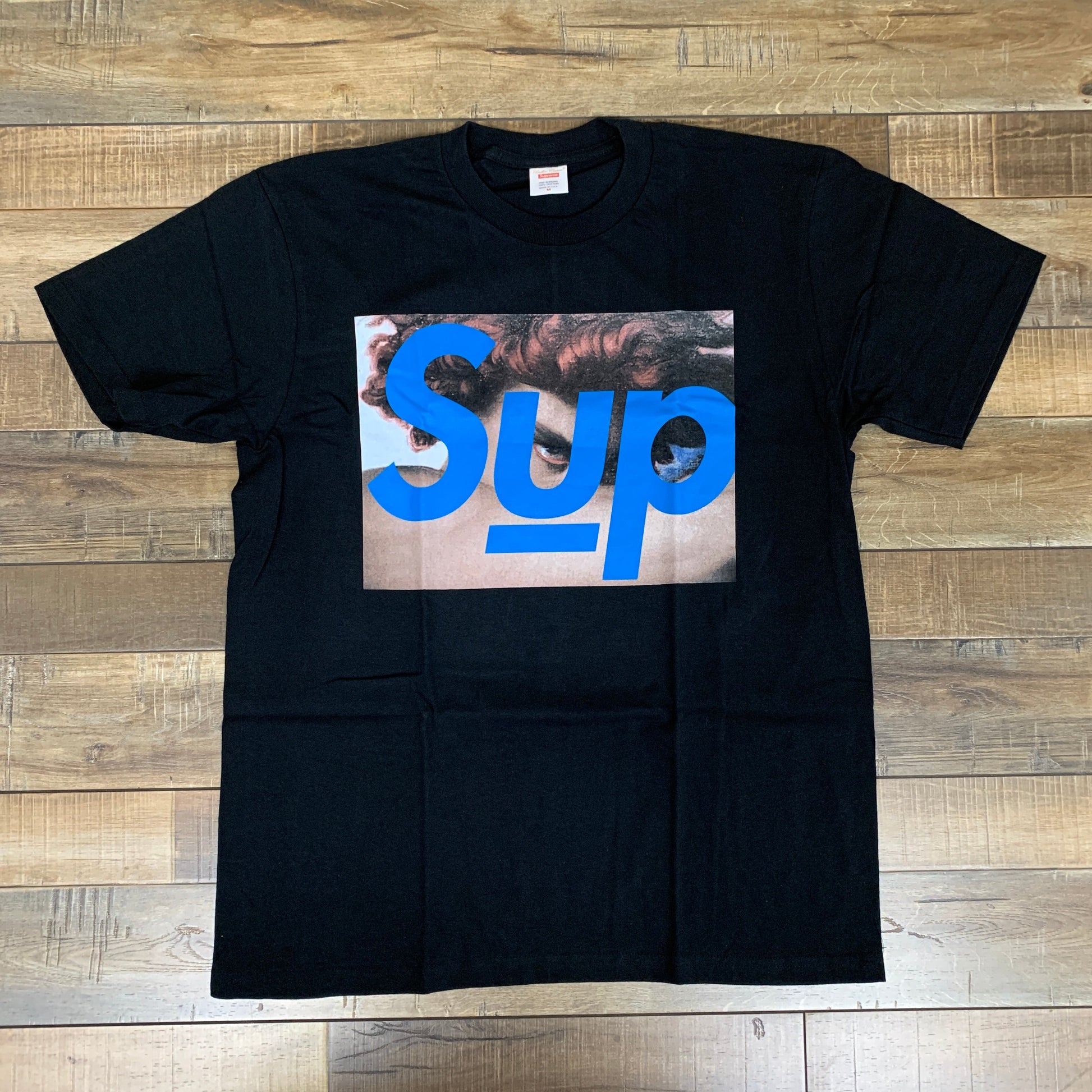 Supreme UNDERCOVER Face Tee Black on wood background.