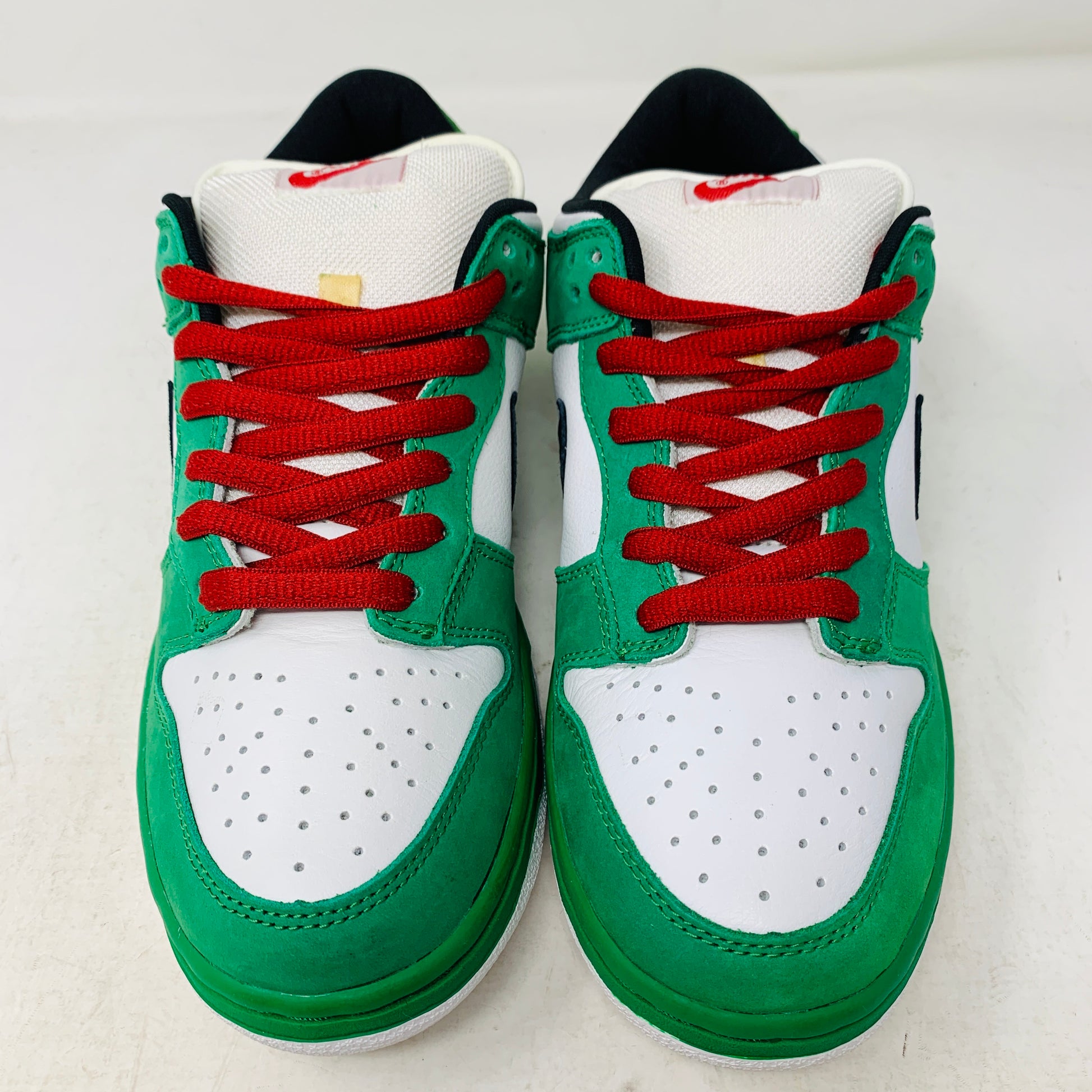 The Nike SB Dunk Low Heineken sneakers feature green and white panels with red laces, a black swoosh on the sides, and a white perforated toe box. They are displayed side by side on a white surface.