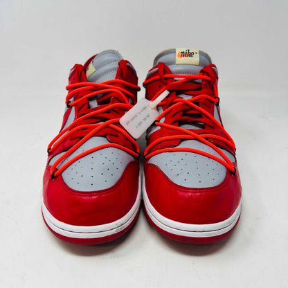 A red and gray Nike Dunk Low Off-White University Red sneaker with orange laces sits atop a shiny silver box. These authentic shoes feature clean uppers, a red swoosh, overlapping lace loops, visible tags, and a unique design.