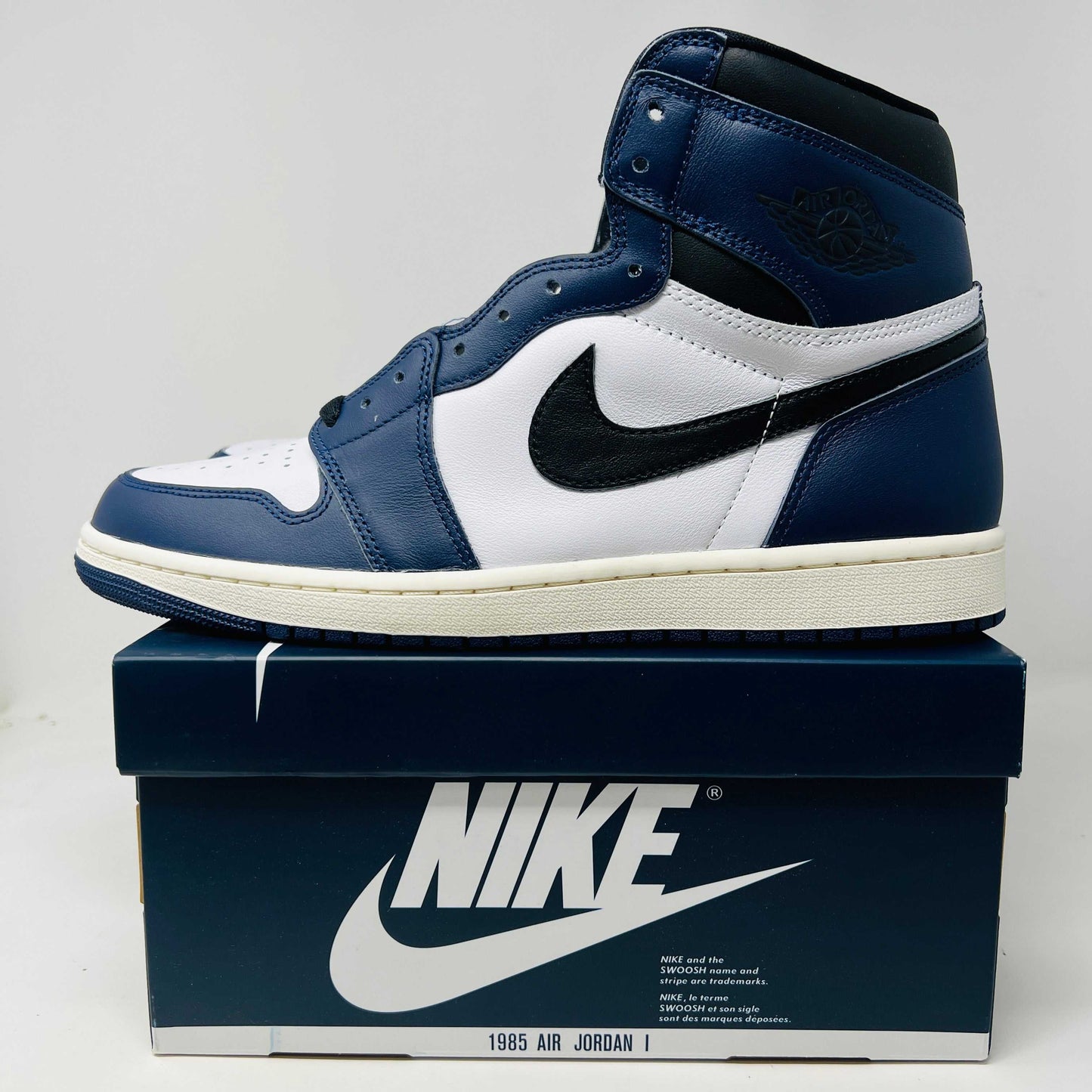 A brand new Jordan 1 Retro High OG Midnight Navy high-top sneaker, featuring navy blue, white, and black colors with the iconic swoosh and Air Jordan logo, displayed on a matching shoe box.