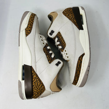 The Jordan 3 Retro Palomino, from the 2023 collection, features clean beige and brown uppers, textured brown accents, white laces, and a white midsole with a visible air unit. Its paired with a unique green and gray patterned replacement box.