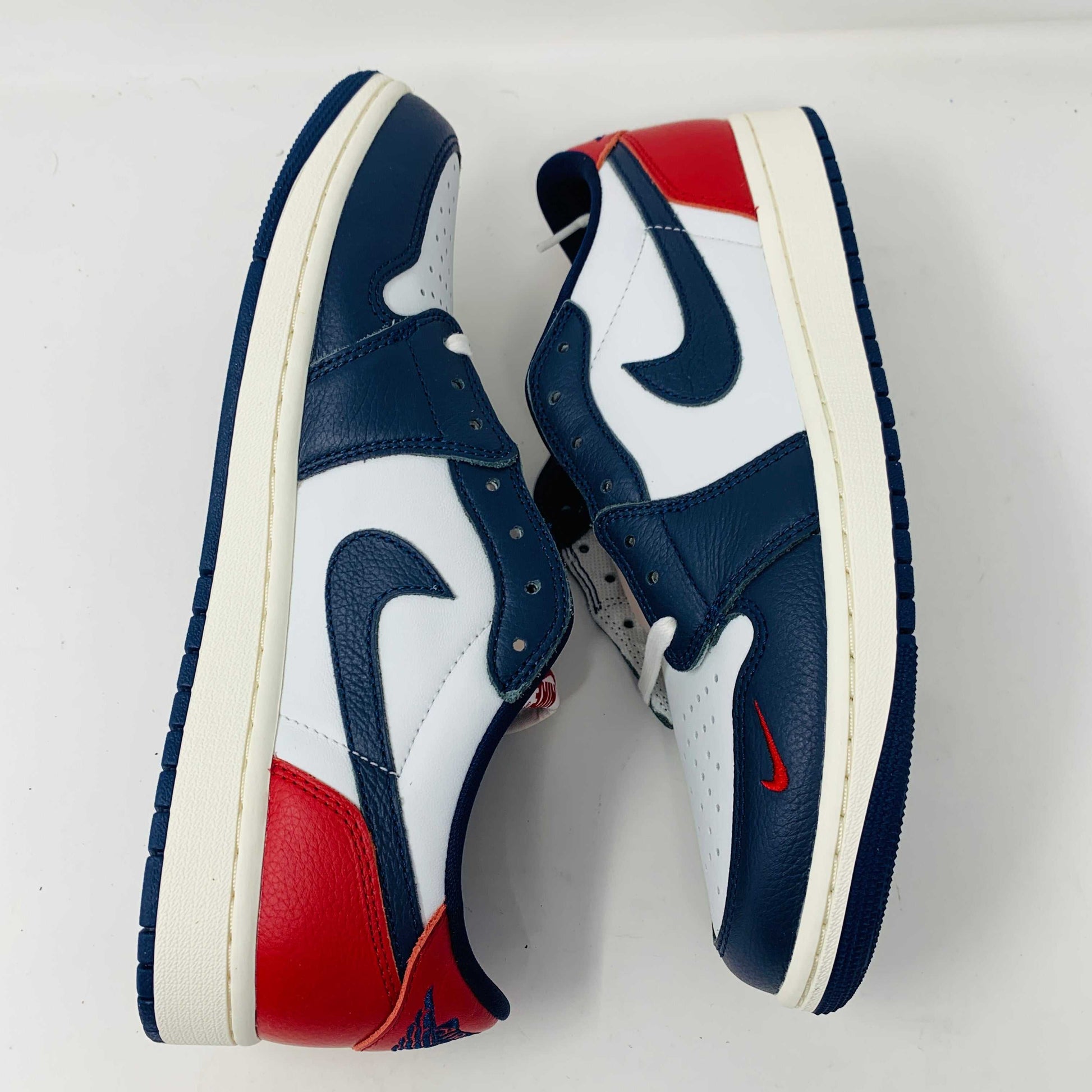 The Jordan 1 Retro Low OG Howard University sneaker, in navy, white, and red with a white midsole and Nike swoosh, rests on the shoe box. A small brown box with extra laces is placed in front.