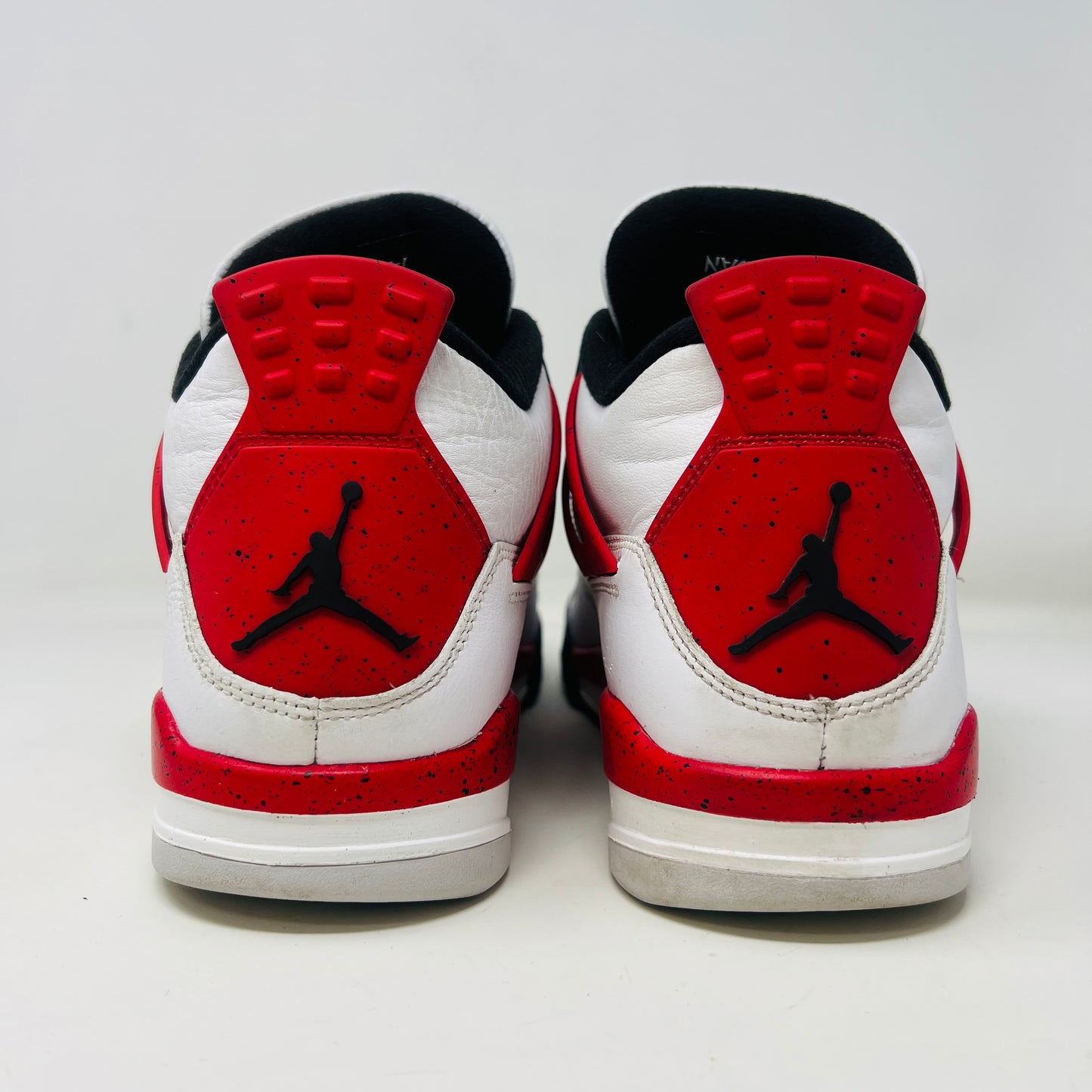 The Jordan 4 Retro Red Cement sneakers, by Jordan, are showcased on their box. They feature authentic white leather, clean uppers with red accents, black netting, and visible air cushioning. The textured box includes a size label.