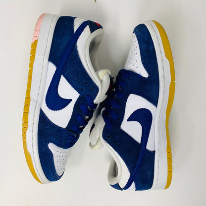 The Nike SB Dunk Low Los Angeles Dodgers sneakers, featuring blue suede and white leather panels with white laces and yellow soles, have a distinctive blue swoosh and a contrasting pink heel section. They are displayed side by side on a white background.