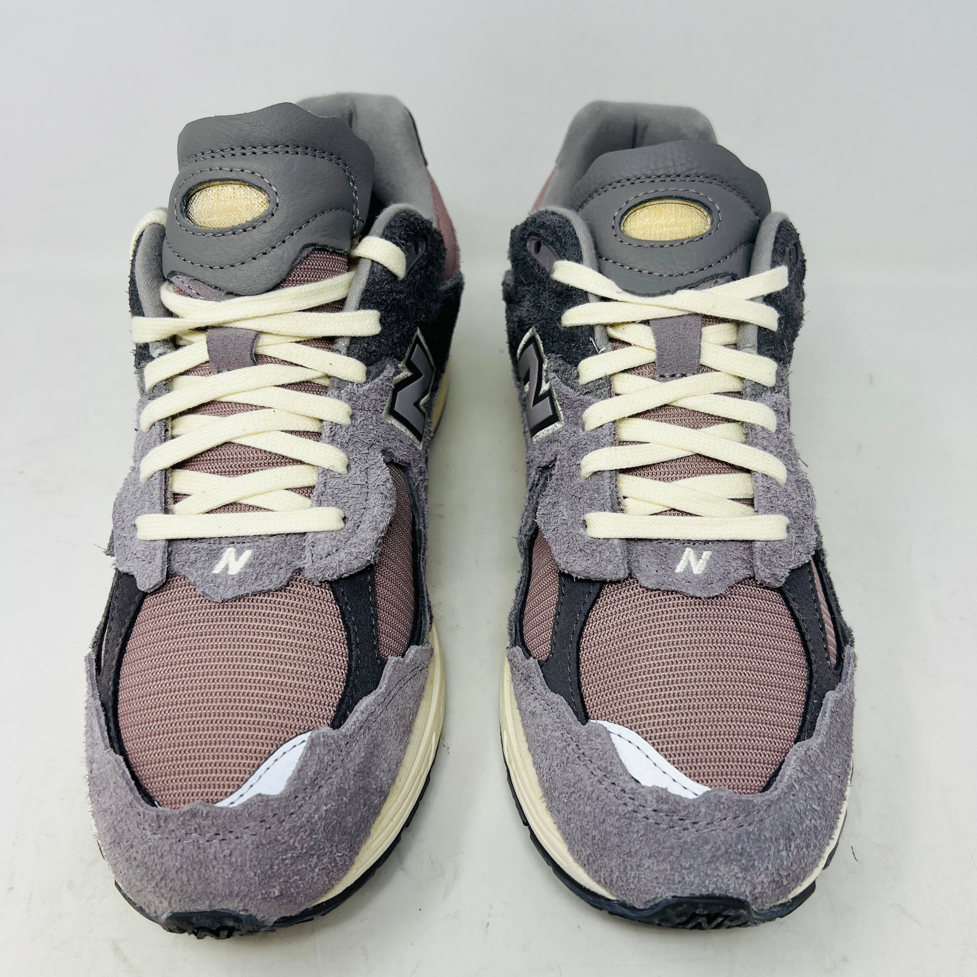 A pair of New Balance 2002R Protection Pack Lunar New Year Dusty Lilac sneakers mix gray and beige tones with CLEAN UPPERS and a textured design. Displayed on a shoebox, they include extra maroon laces. The box label details the shoe size and model.