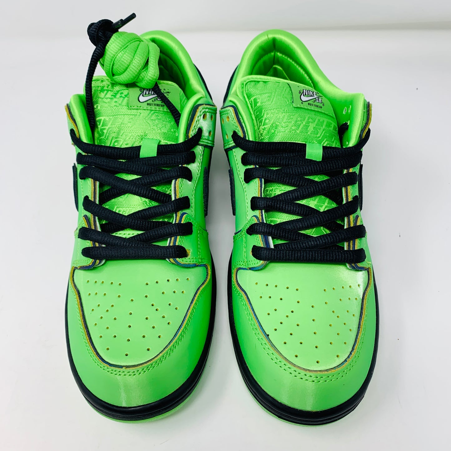 The Nike SB Dunk Low The Powerpuff Girls Buttercup sneakers are vibrant green with black laces and accents, featuring a textured tongue. They are displayed side by side on a white background.