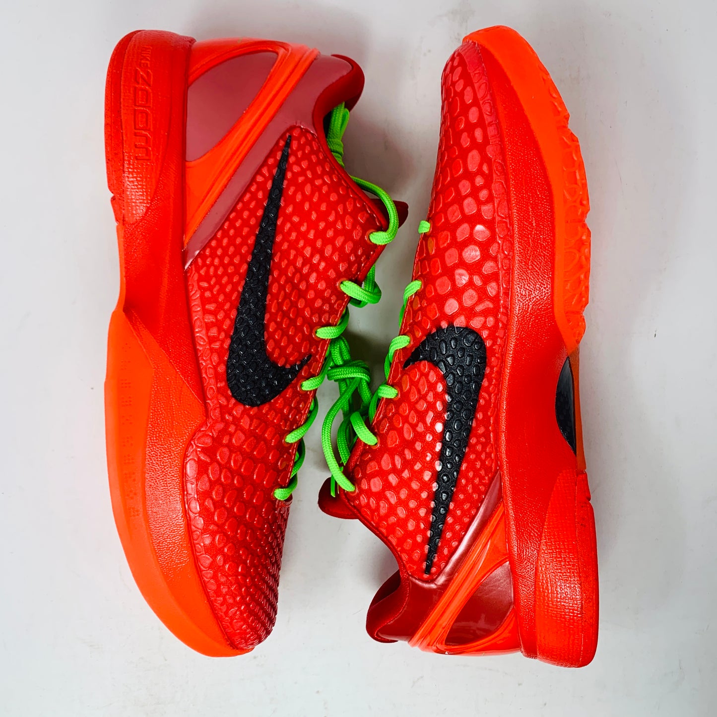 The Nike Kobe 6 Protro Reverse Grinch features a vibrant red colorway with black swoosh logos and bright green laces. Displayed on a white background, these athletic basketball shoes have soles and heel areas matching the bold red hue.