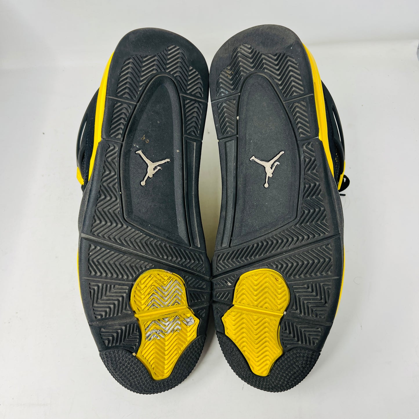 The Jordan 4 Retro Thunder (2023) features black uppers with yellow accents, a white sole, and visible air cushioning. It rests on a black and gray speckled shoebox in good condition and includes the distinctive wing design.