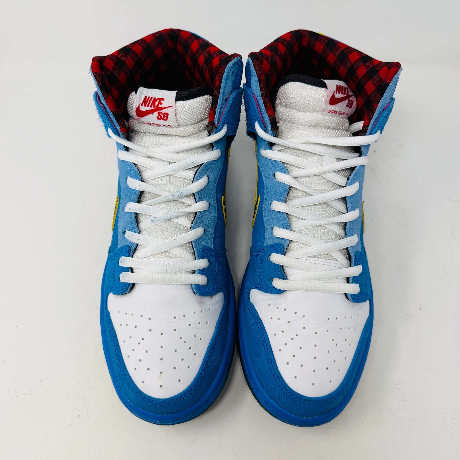 The Nike SB Dunk High Familia Blue Ox, a 2015 release by Nike, features clean blue uppers with a yellow swoosh, decorative stitching, red and black checkered lining, lace-up front, and an edgy skull with crossed bones on the side—its standout design loses no stars.