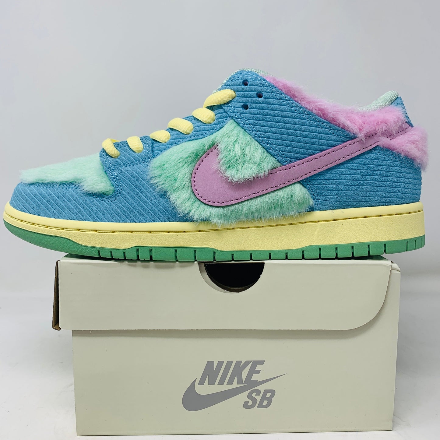 The Nike SB Dunk Low Verdy Visty sneaker showcases blue, pink, and mint green furry panels, a light purple swoosh, yellow laces, and a vibrant green and yellow sole, all on an authentic Nike SB shoe box.