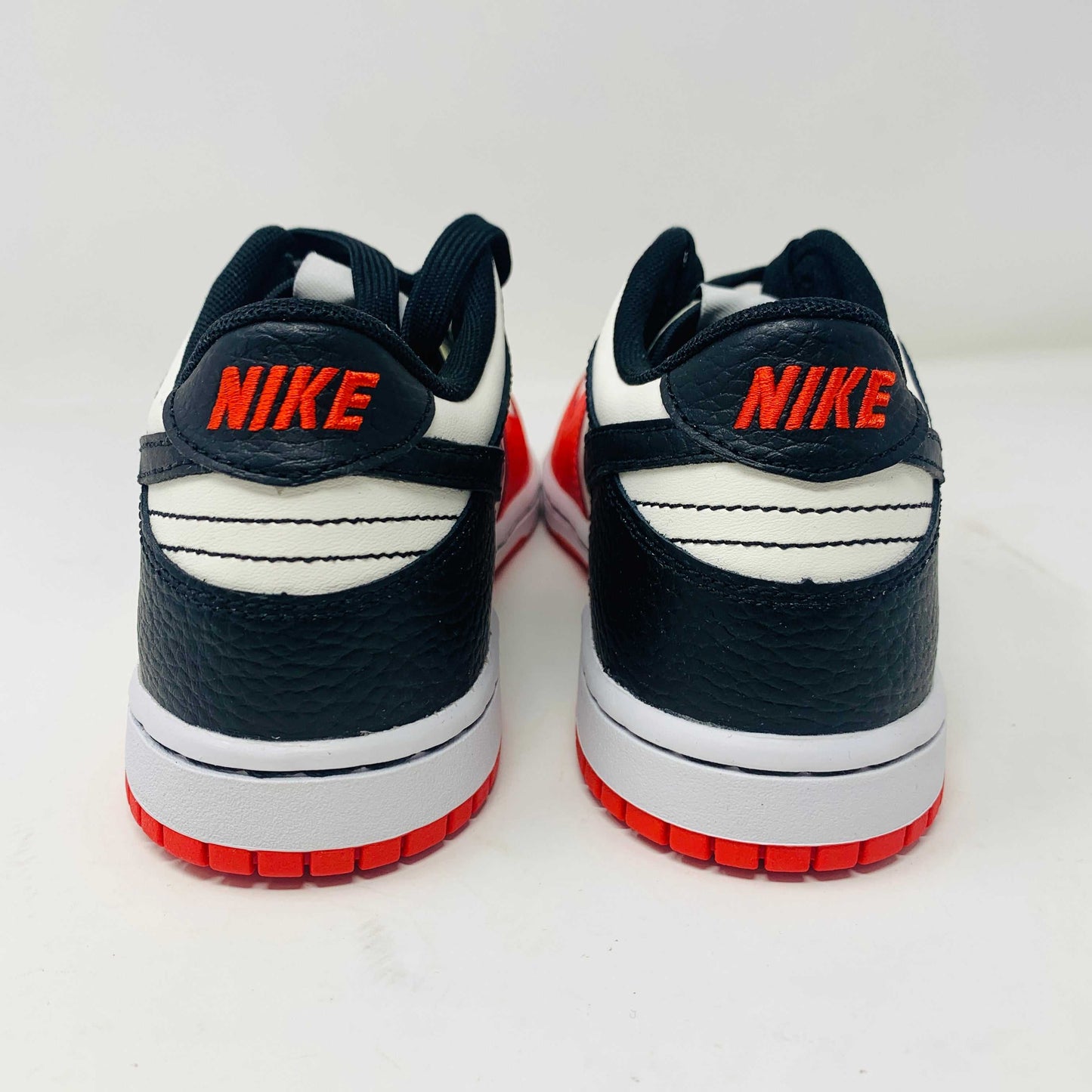 The Nike Dunk Low EMB Chicago GS, a genuine pair of red, black, and white sneakers featuring a sleek black swoosh and matching laces, elegantly sits atop a new red box adorned with bold white Nike branding.