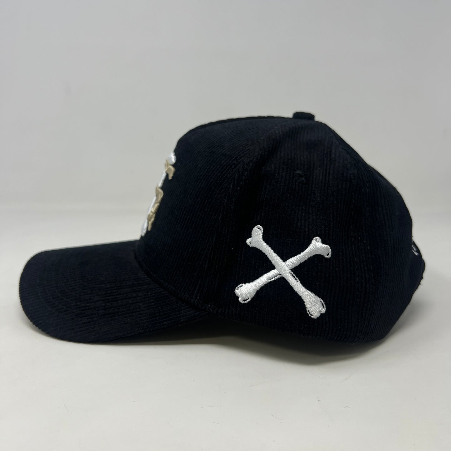 The Holy Ground Bones Hat Corduroy Black by Holy Ground features a ribbed texture, an embroidered crossed bones and A & B design, and a side white X. Its one-size ensures universal fit.