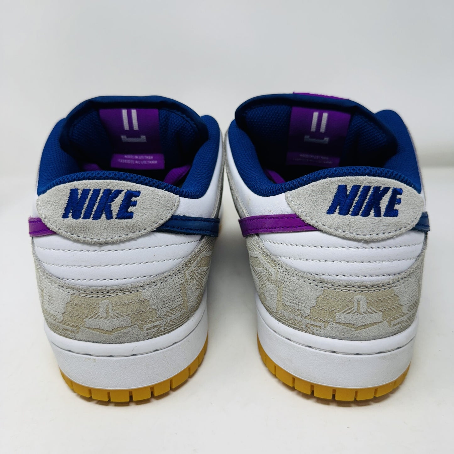 The Nike SB Dunk Low Rayssa Leal sneakers, shown from the back on a white background, feature clean uppers in white, beige, and blue with purple accents. The iconic Nike logo is on the heel and theyre finished with a stylish gum sole.