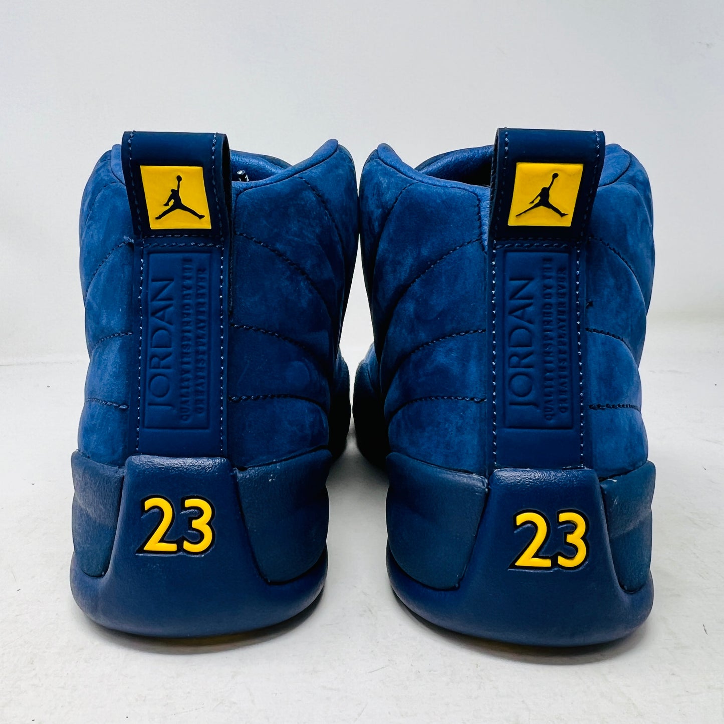 The Jordan 12 Retro Michigan is a blue high-top sneaker with yellow accents from Jordans 2018 Shoes collection. It features a textured surface, stitching details, and a visible Jumpman label. The dark blue sole highlights its vibrant design against a white background.