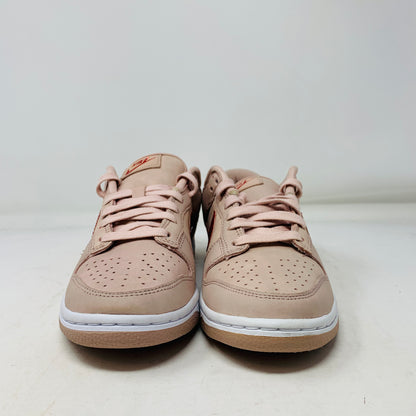 A pair of Nike Dunk Low PRM Pink Oxford (W) sneakers, featuring light pink color with white midsoles and tan outsoles, are placed side by side on a white surface. They have laces and a logo patch on the tongue.