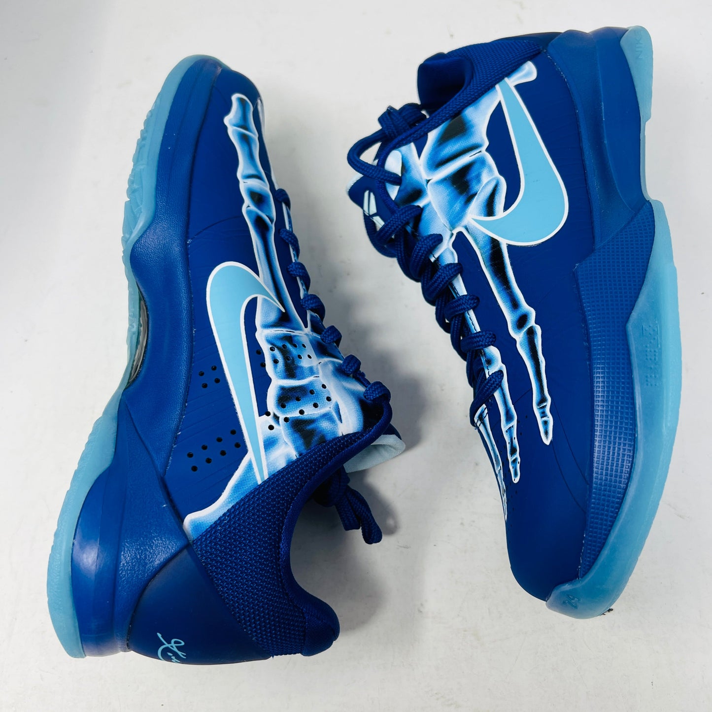 The Nike Kobe 5 X-Ray (GS) athletic shoes feature a light blue skeletal design and a Nike swoosh on the sides, shown against a white background.